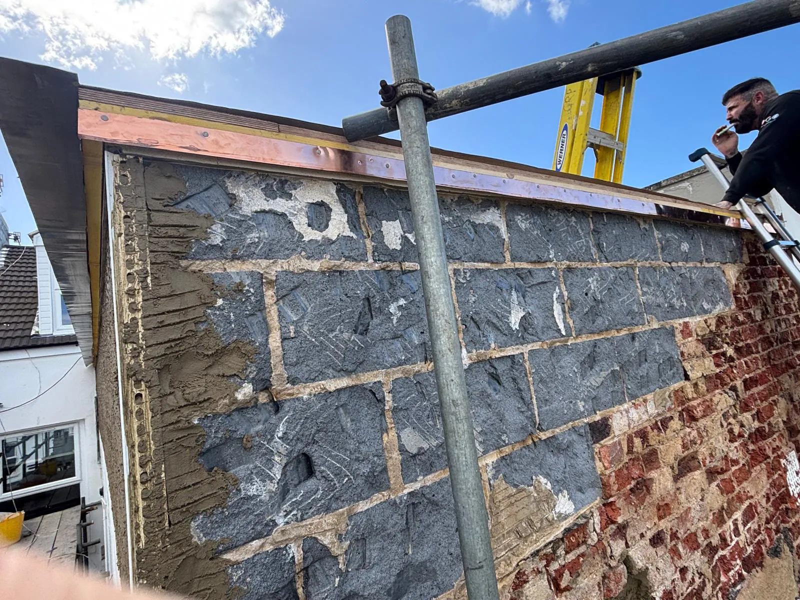 Outer face of the balcony wall exposed with the coping removed — blockwork visible from the scaffold