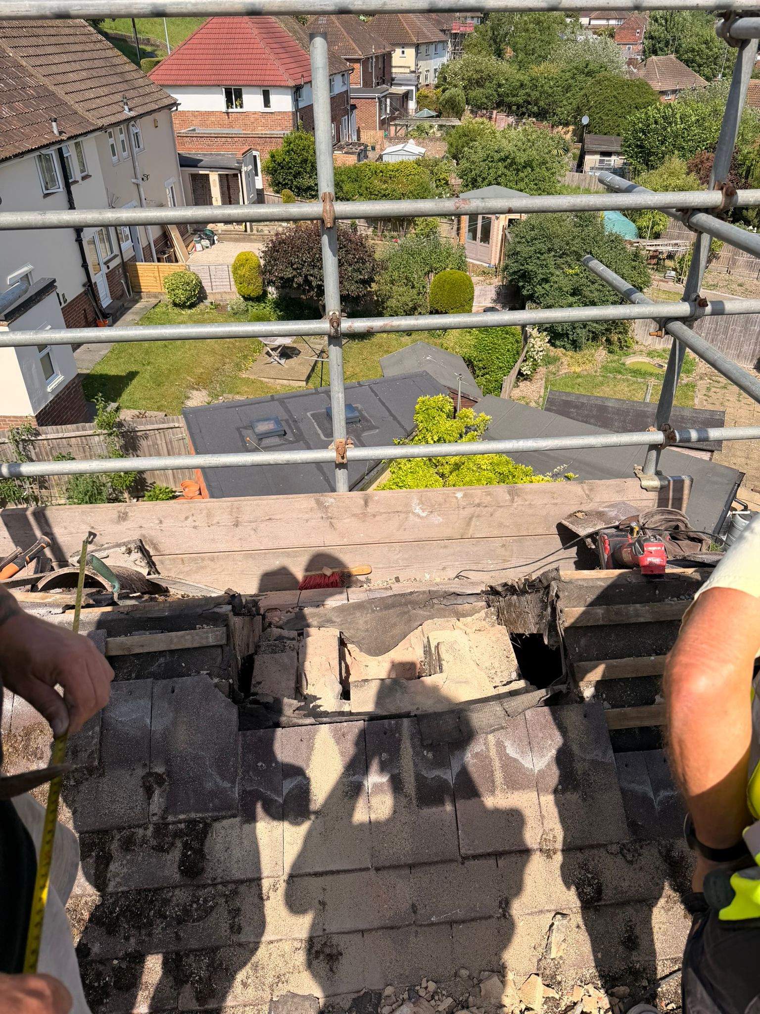 Two workers measuring up at the open chimney void on Heath Hill Avenue, Bevendean — stack just removed and tiles stripped back ready for structural work