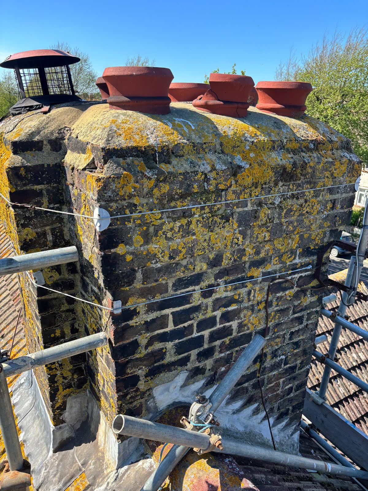 Heavily weathered chimney stack on a Portslade property before restoration — lichen and moss growth across the brickwork and deteriorated mortar joints, scaffolding erected