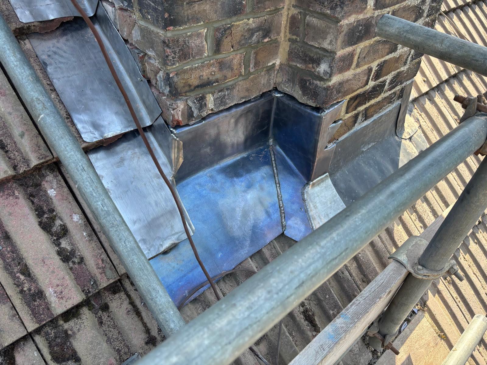 Fabricated lead soaker tray and back gutter installed at the chimney base — welded lead gutter collecting water from behind the stack and directing it away from the roof