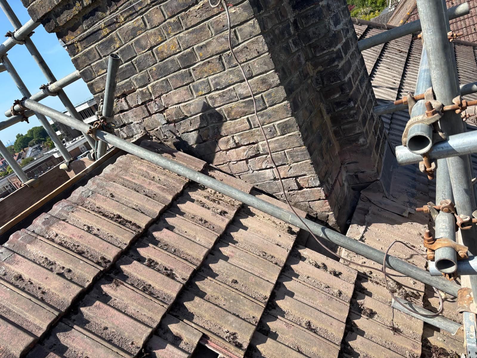 Repointed chimney stack detail showing the scaffold base — fresh mortar joints throughout and old weathered pointing fully removed and replaced