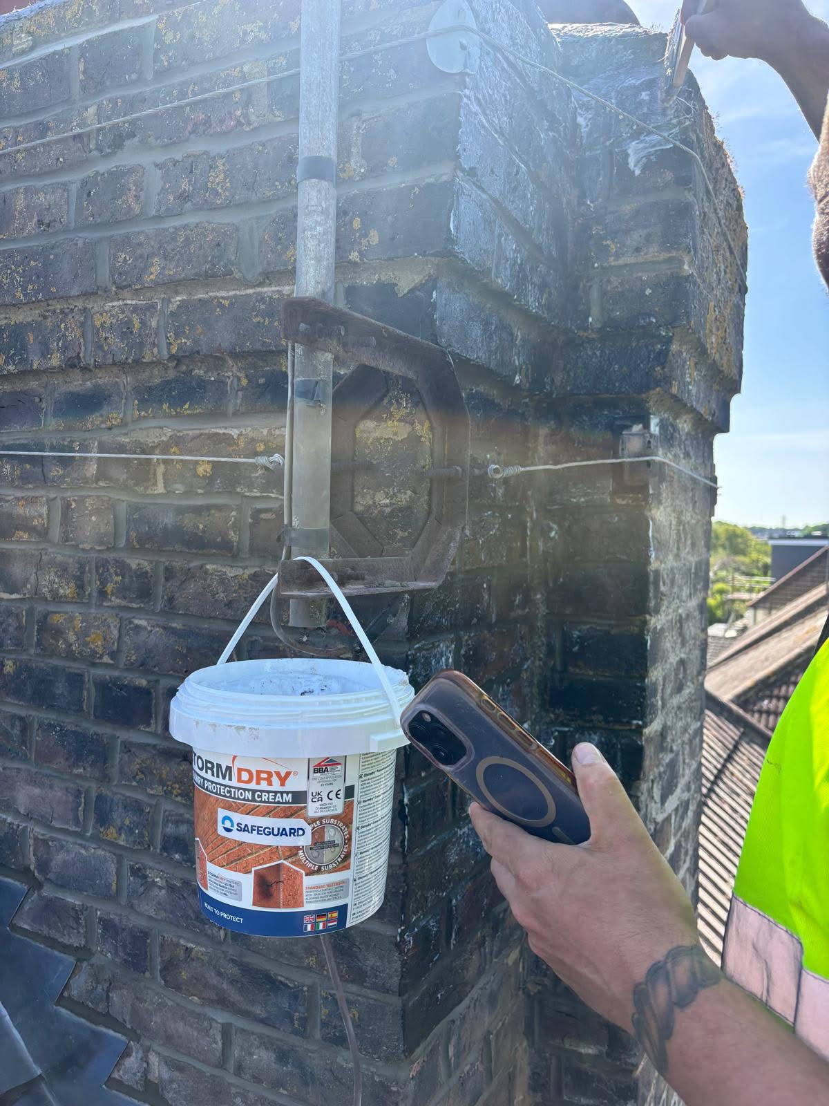 Stormdry masonry protection cream being applied to the repointed chimney stack — breathable water-repellent treatment to seal and protect the brickwork as the final stage of restoration