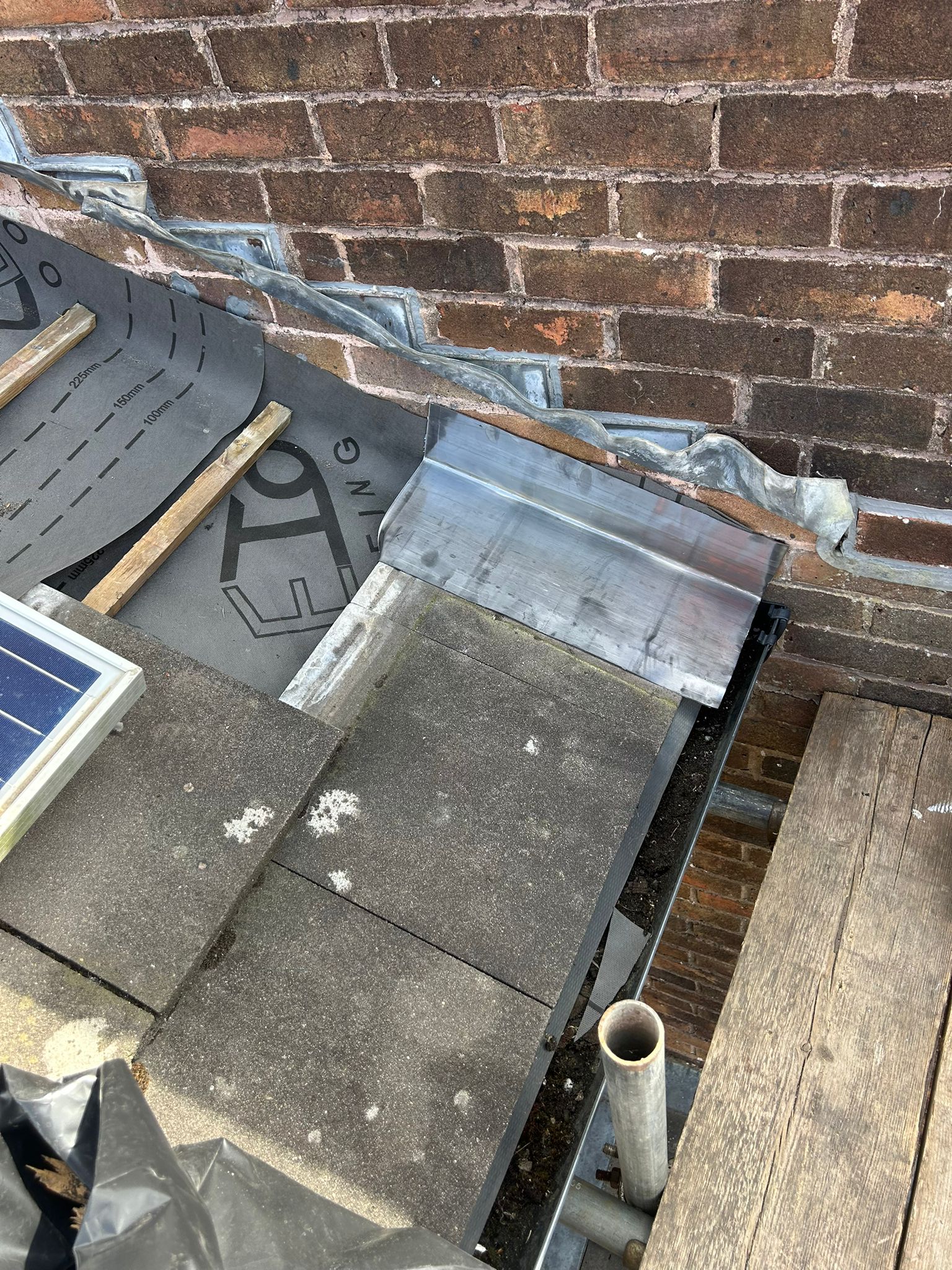 Close-up of the junction between the roof and adjoining wall during flashing strip-out — old lead removed and deck exposed ready for new soakers