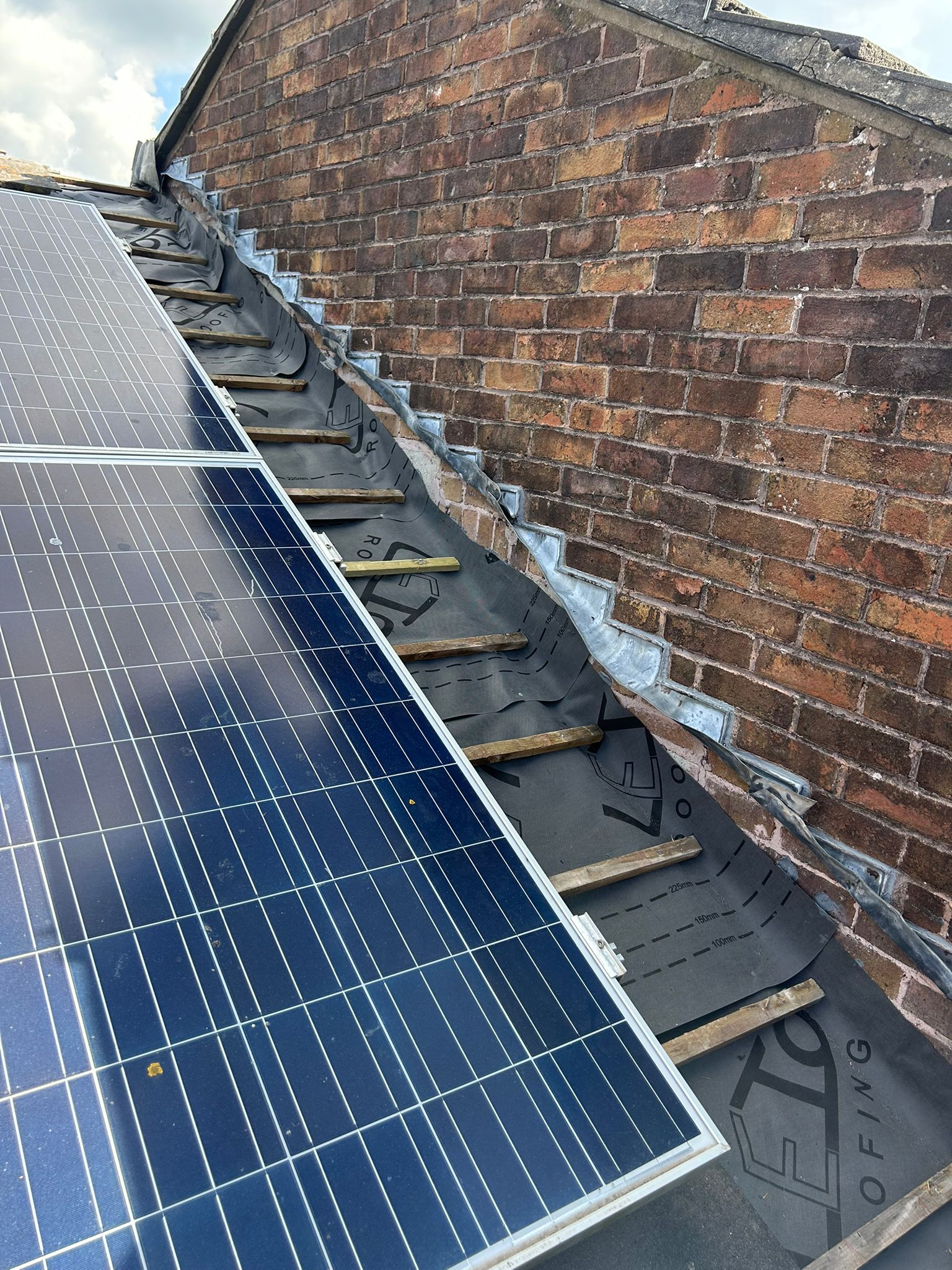Roof tiles and solar panels on a Whitehawk Brighton property with old flashings stripped back against the adjoining brick wall — start of works