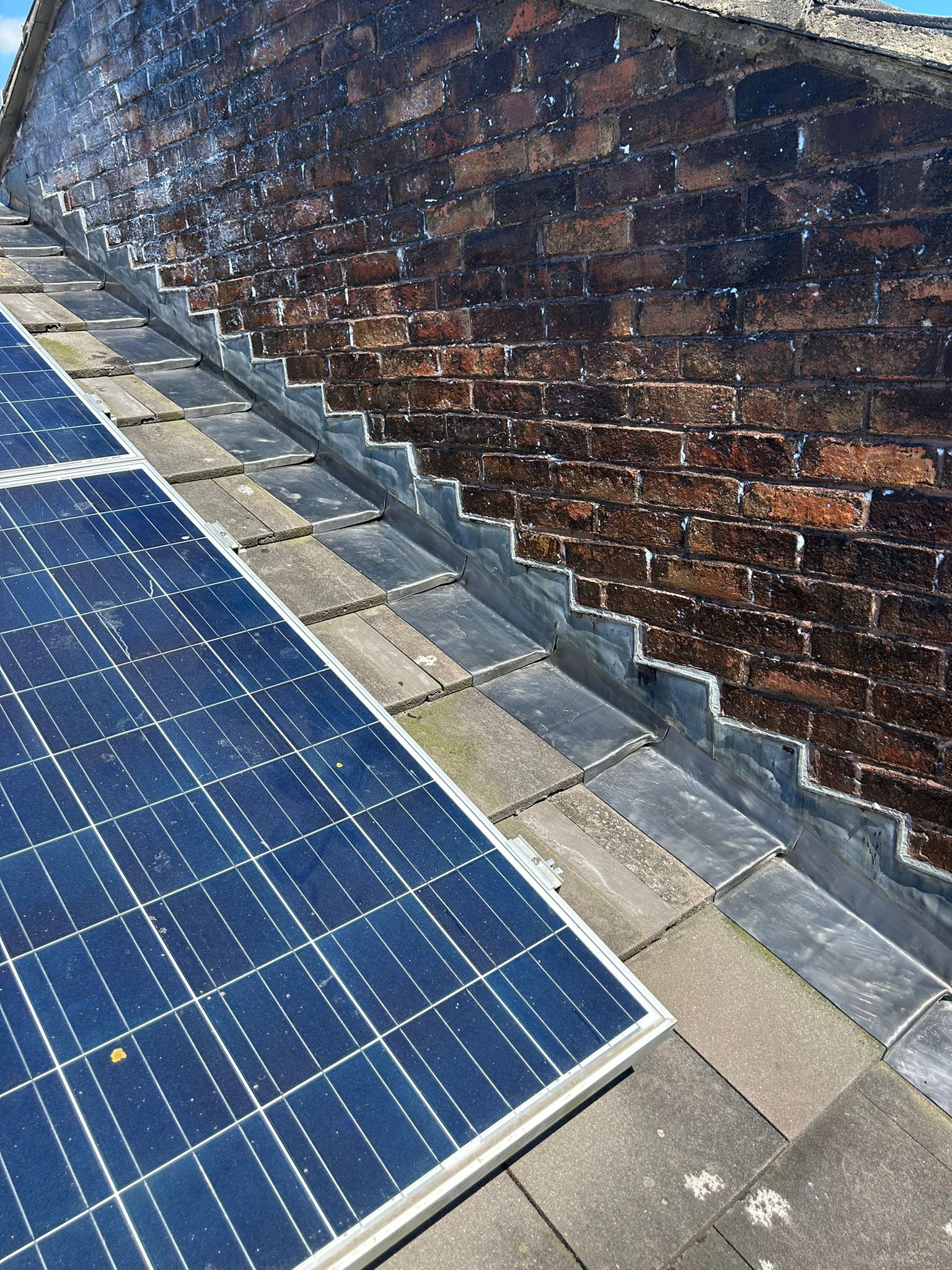 Completed lead soaker flashings running the full length of the roof abutment in Whitehawk — individual soakers clearly visible stepping up with each tile course