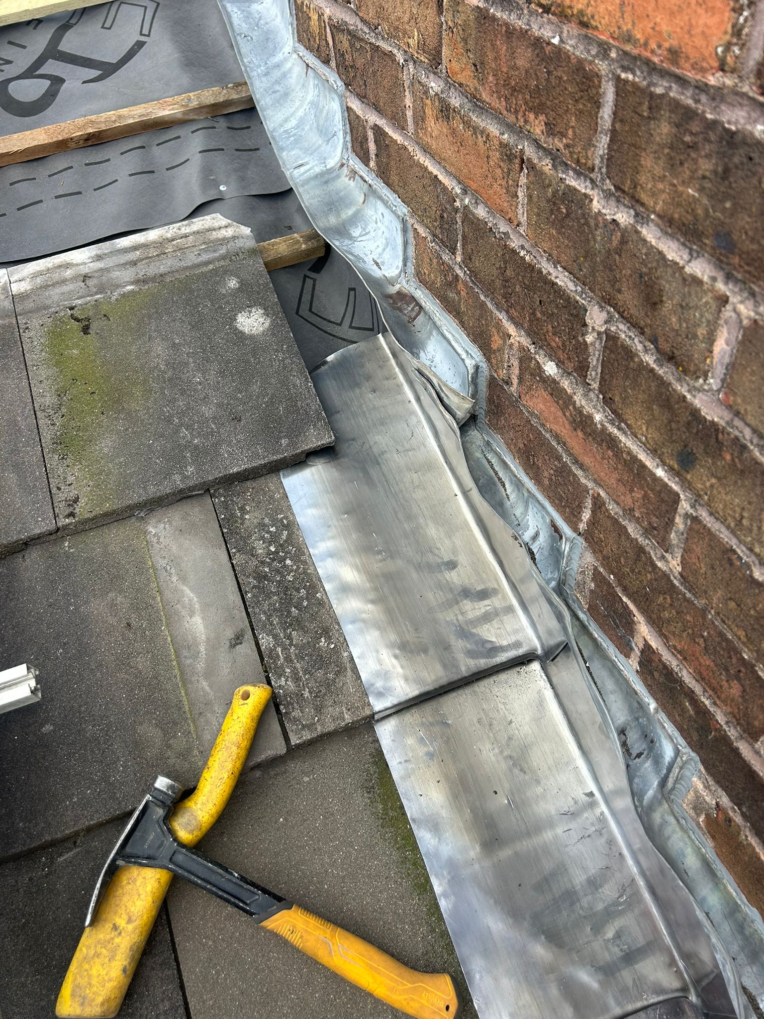 Individual lead soakers being fitted between roof tiles and the adjoining wall in Whitehawk — soakers installed course by course up the slope