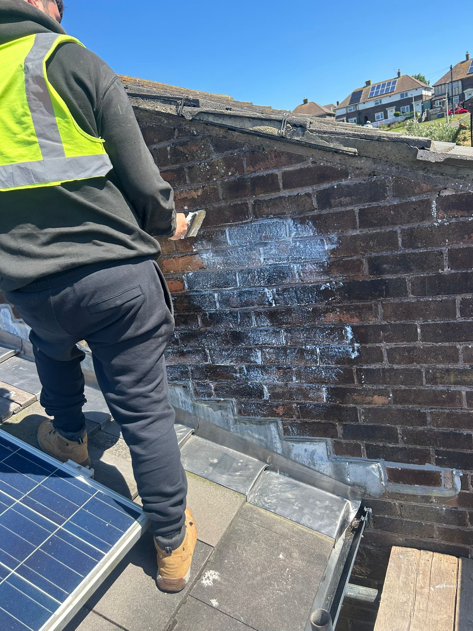 Stormdry masonry protection cream being applied to the adjoining brick wall in Whitehawk — breathable water-repellent treatment brushed into the brickwork above the new flashings