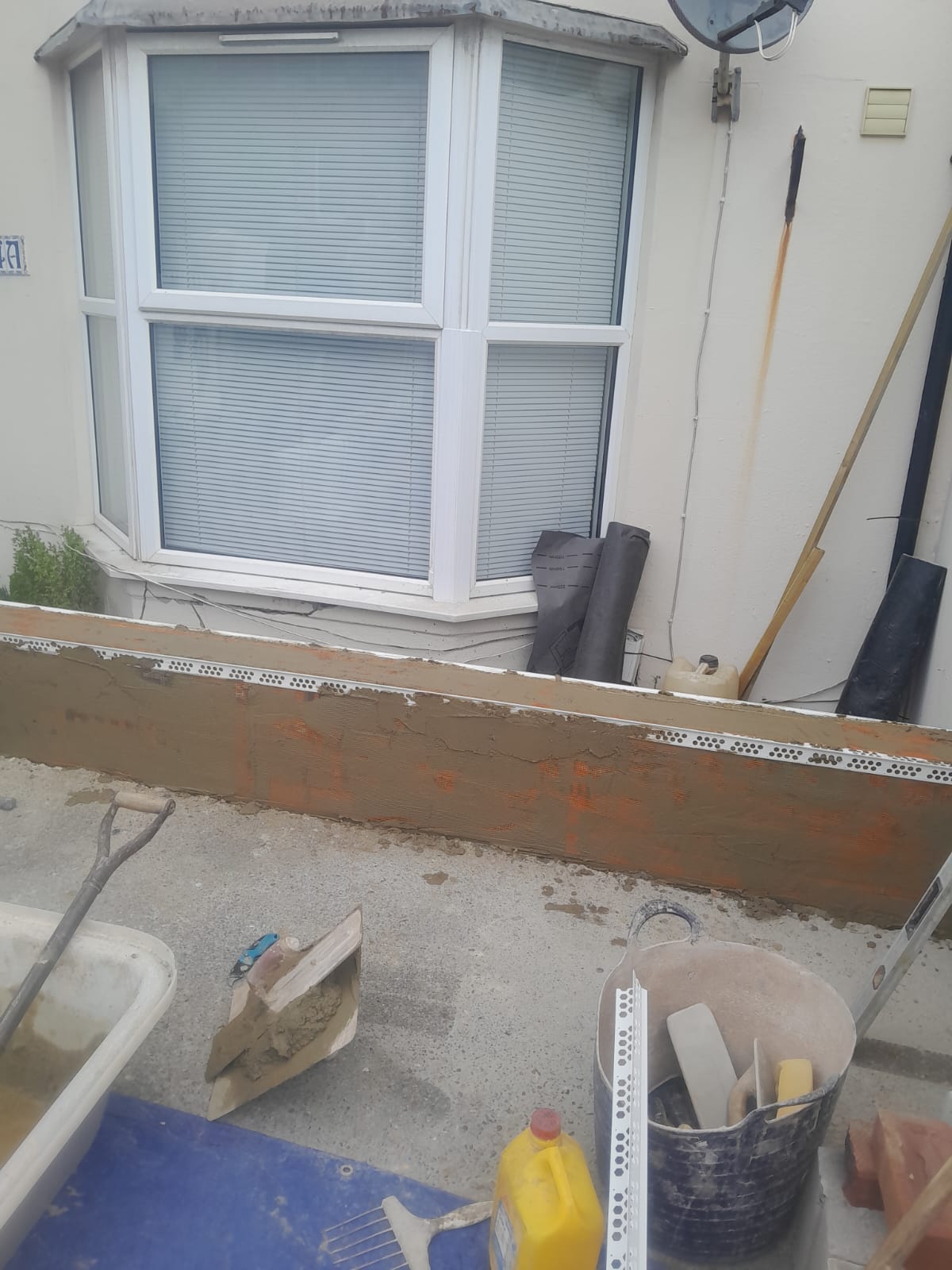Render being applied to rebuilt wall — work in progress with tools and materials on site